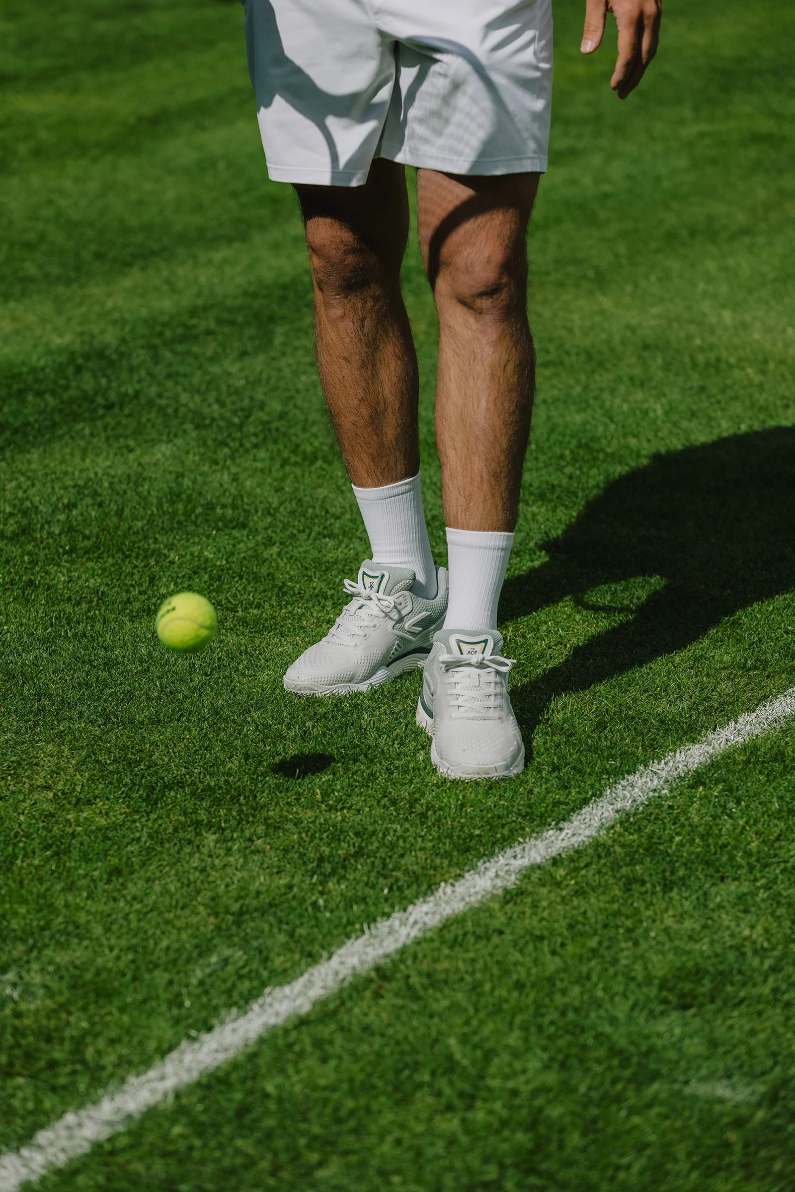 The ACE Hub Johnny Loco performance tennis shoes in off-white and cucumber, worn on a grass court during play.