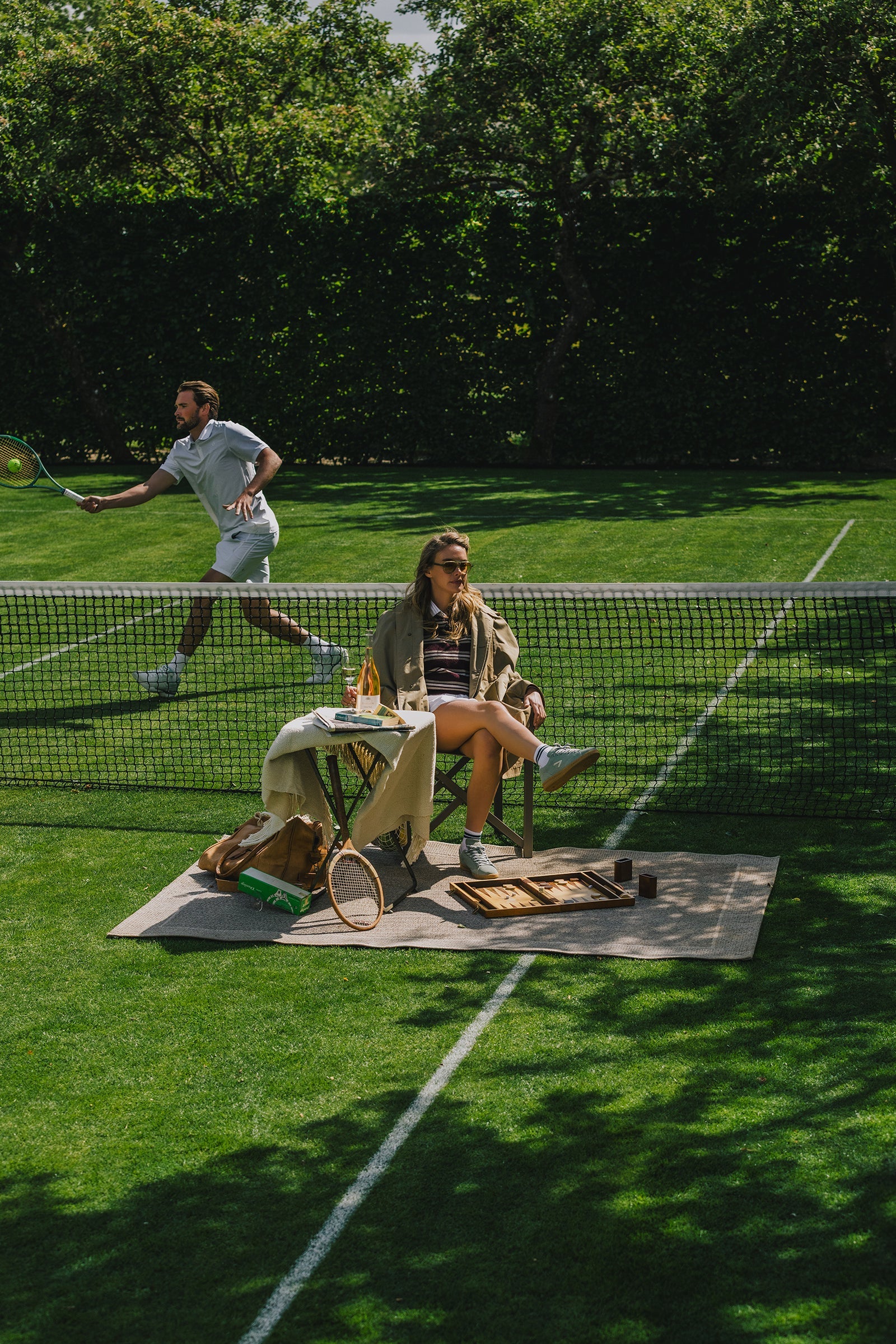 The ACE Hub Johnny Loco collection styled on a grass tennis court, with one player in action and another seated beside vintage tennis gear.