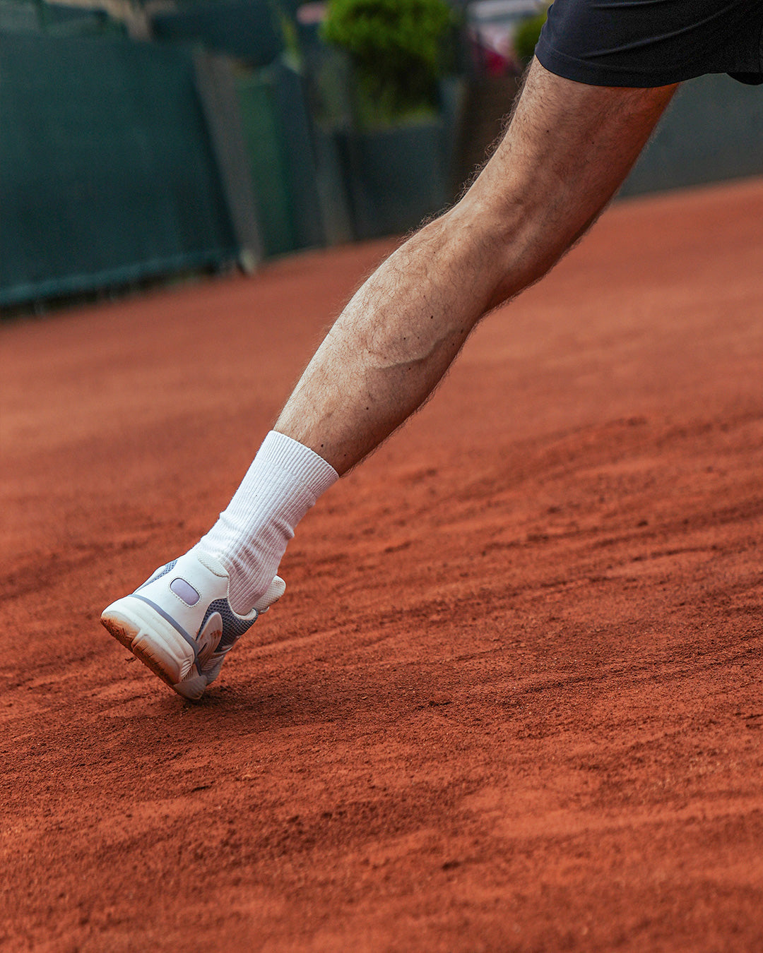 The ACE Hub OC sneaker in sea ice and white, captured mid-movement on a clay tennis court.