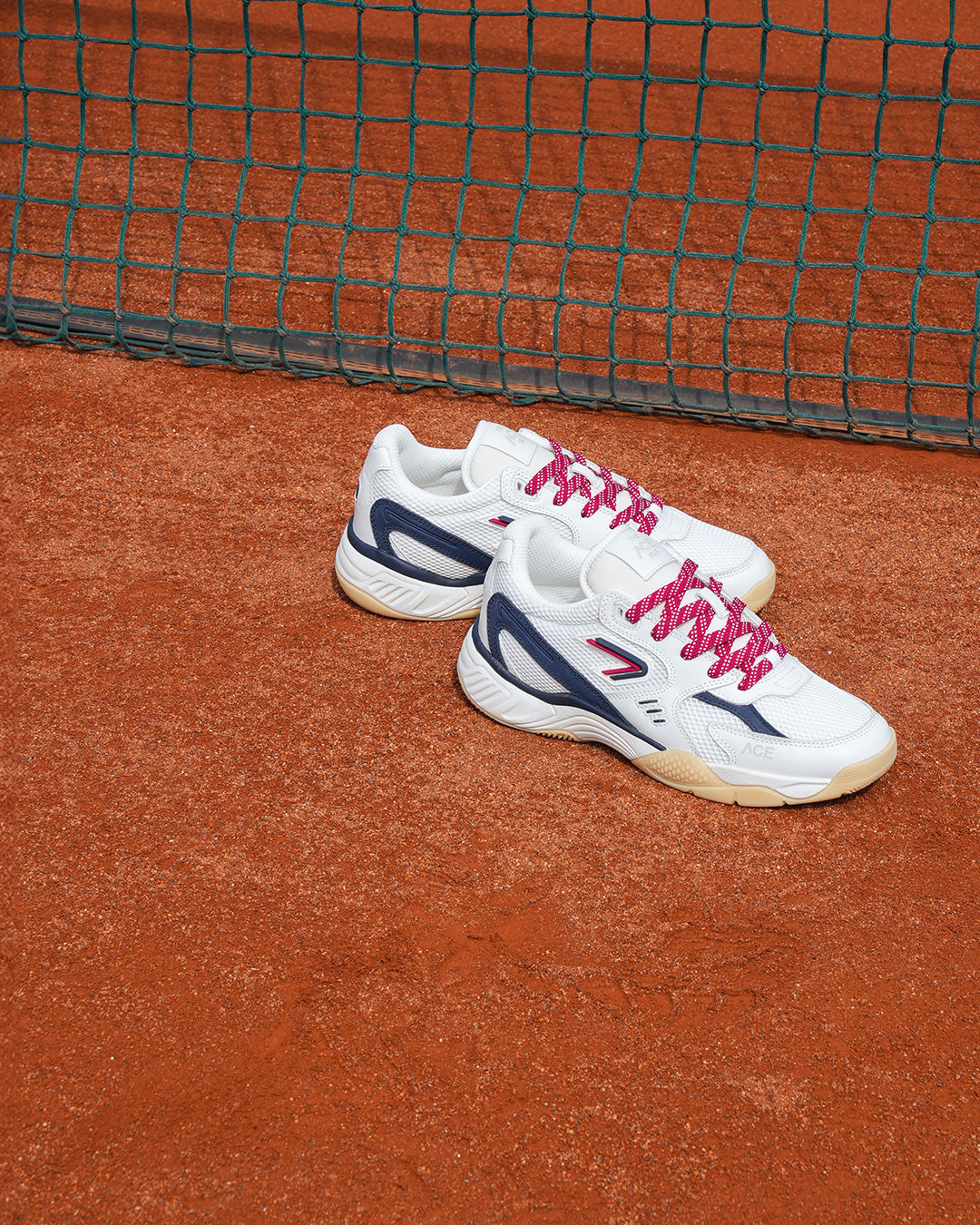 The ACE Hub ACE25 sneaker in white and navy, photographed on a clay tennis court.