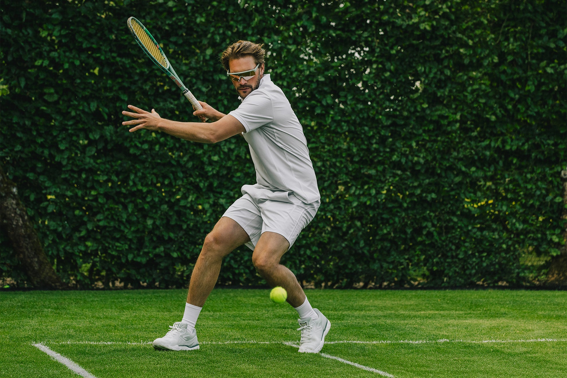 The ACE Hub Performance Johnny Loco sneaker in off-white and cucumber, worn on a grass tennis court.