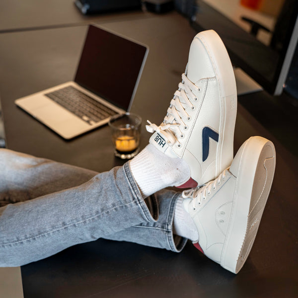 White sneakers the hub logo on a desk with a laptop and glass of coffee.