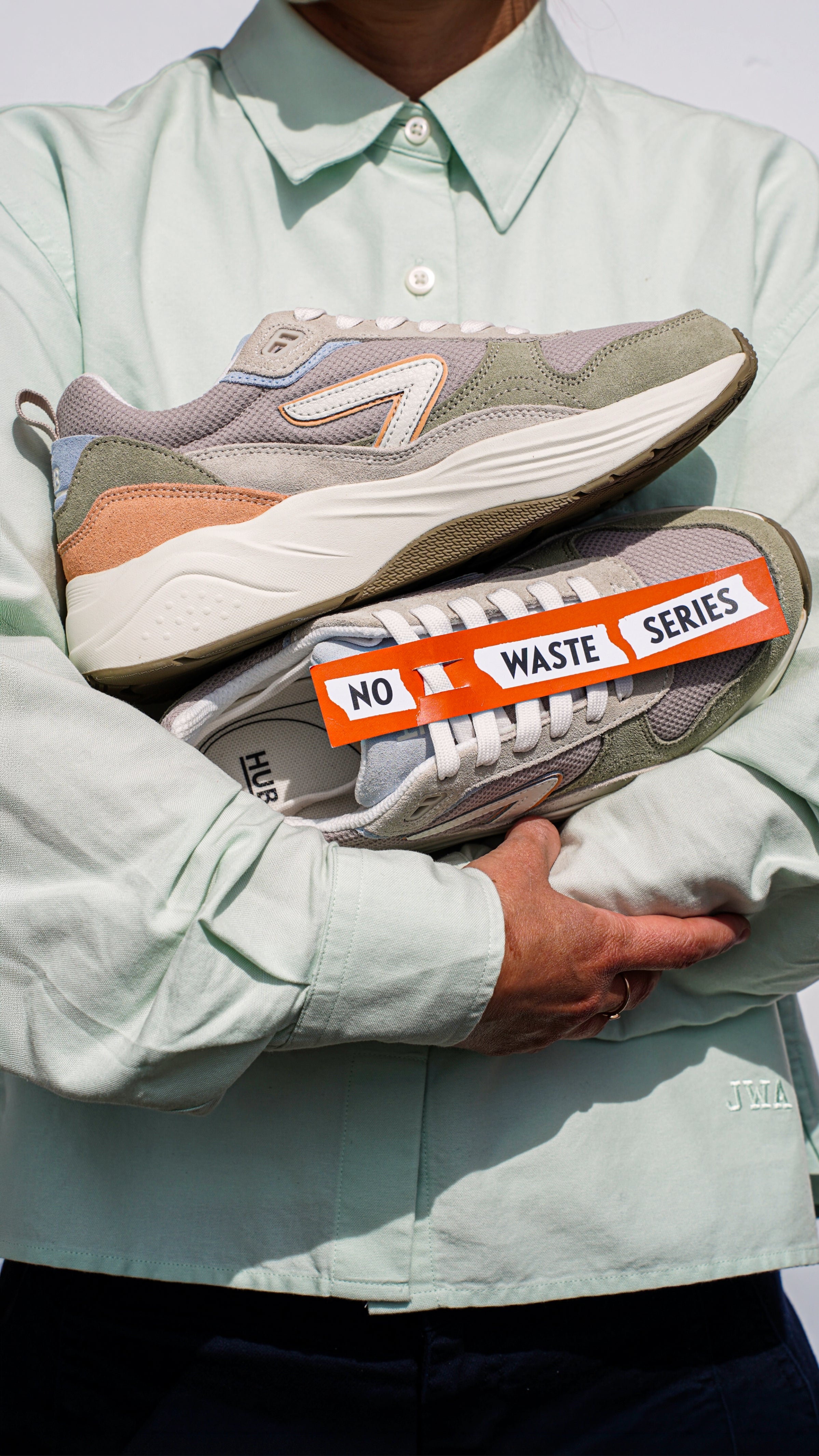Person holding two sneakers with 'No Waste Series' label, wearing a light green shirt.