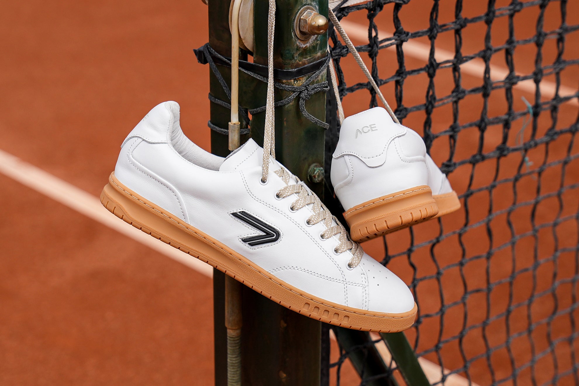 The ACE Hub Shot sneaker, hanging on a clay tennis court net.
