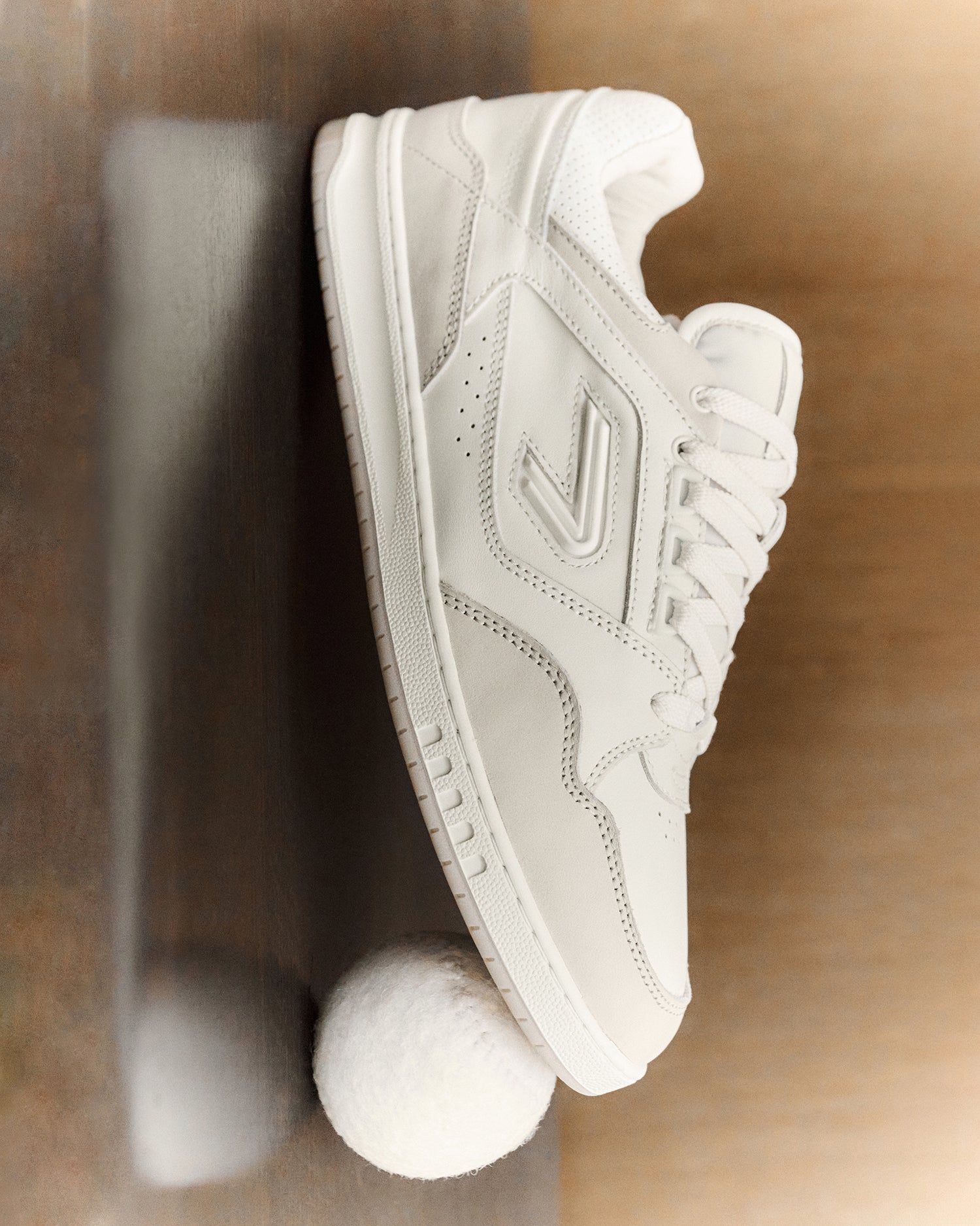 The ACE Hub Sprint sneaker in off-white and white, photographed with a white tennis ball on a wooden surface.