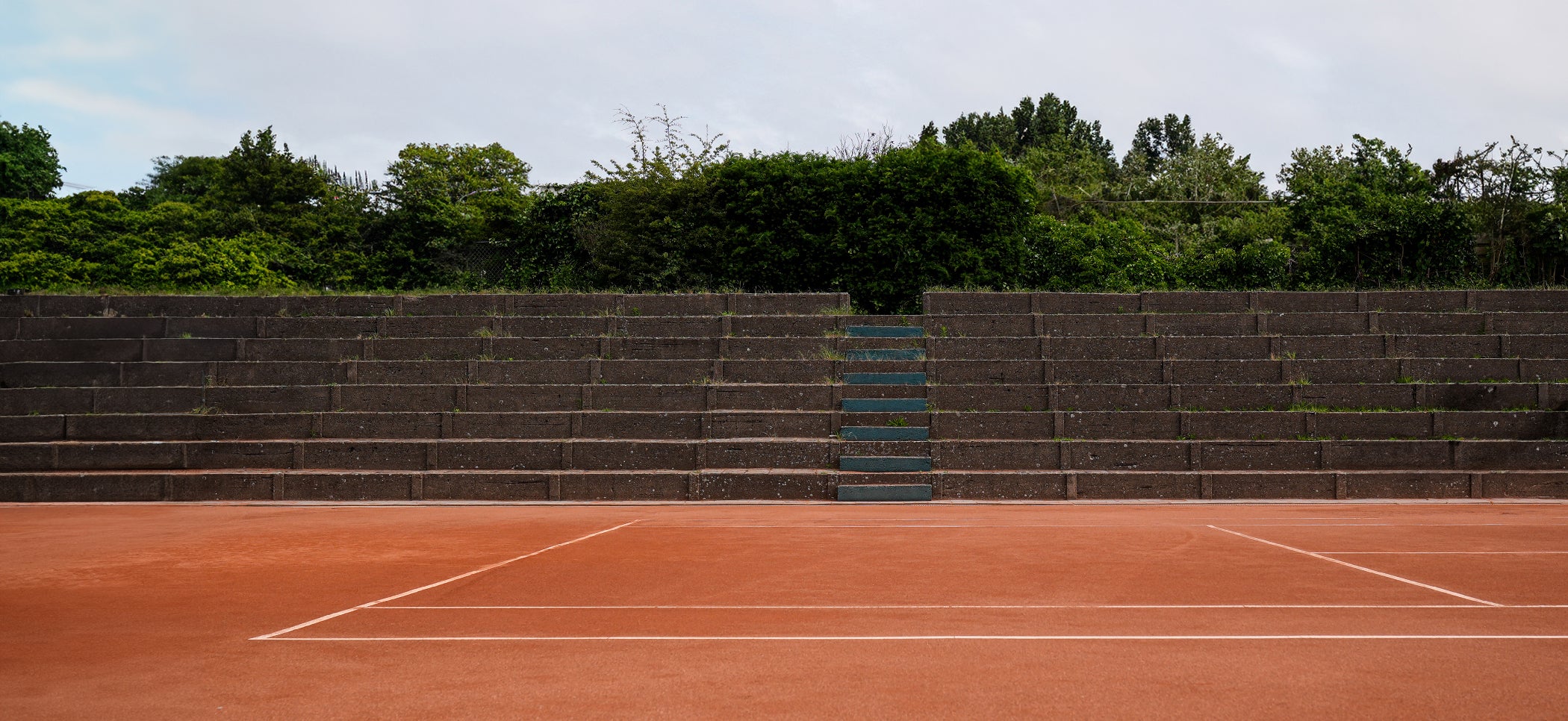 Vintage clay tennis court with weathered concrete stands, part of The ACE Hub Heritage series.