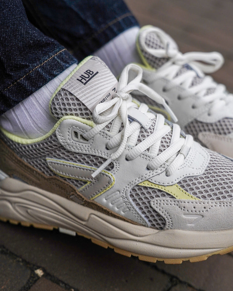 White HUB running shoes with gray mesh and yellow accents worn by a person on a the street