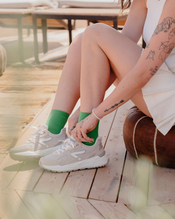 Person wearing green socks and gray HUB sneakers on a wooden deck.

