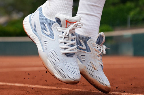 the ACE hub performance tennis shoe in blue on gravel court